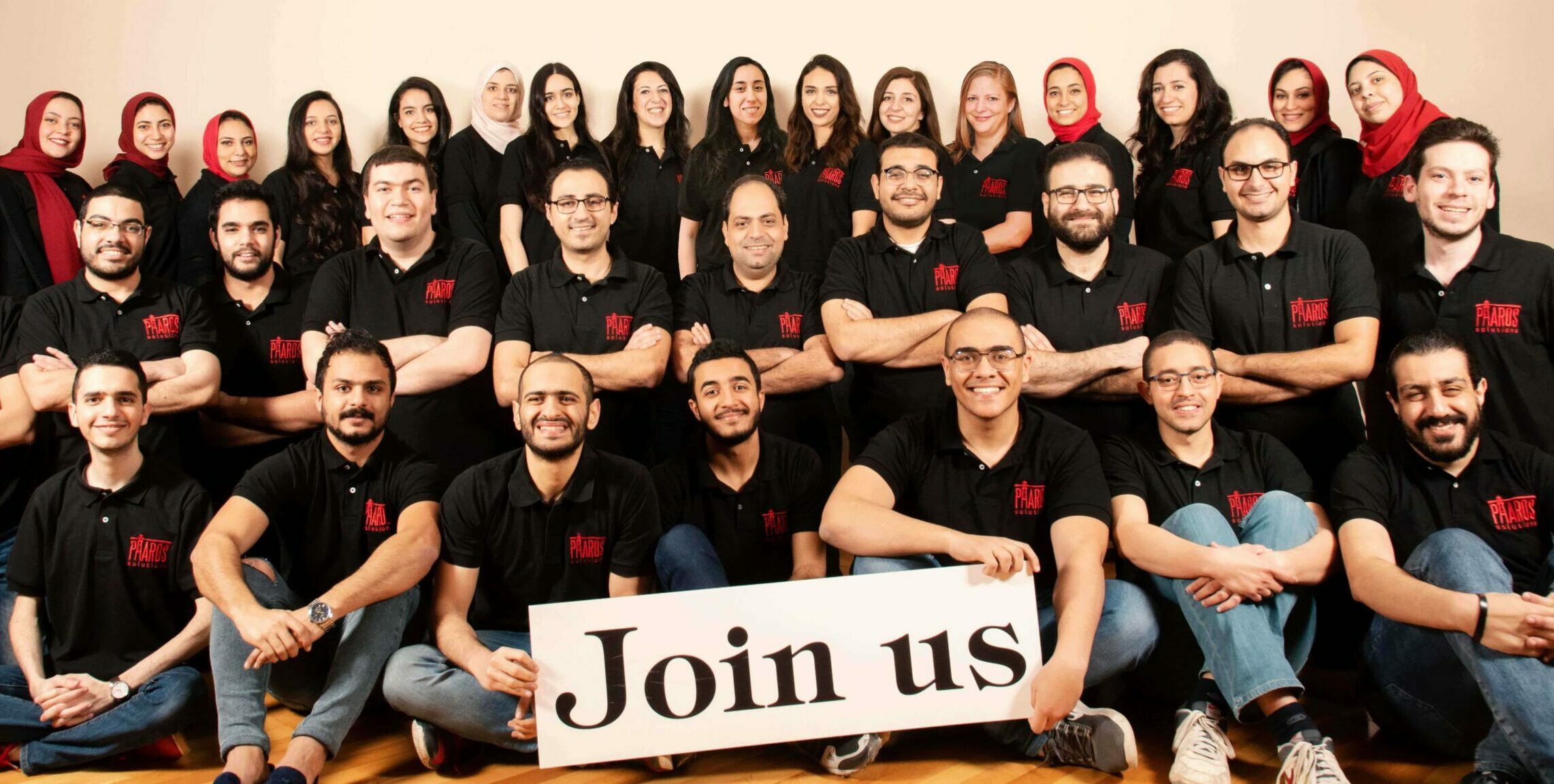 Team of software engineers working at Pharos Solutions holding a sign that says join us to work in a well-established software development company